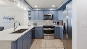 A modern kitchen with blue cabinets, stainless steel appliances, a herringbone tile backsplash, and recessed ceiling lights. - Beachfront Townhouse w/ Modern Upgrades Shared Pool, Fast WiFi, Outdoor Shower (Panama City Beach)
