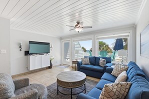 A spacious living room with a large blue sofa, a round coffee table, and a ceiling fan. - Beachfront Townhouse w/ Modern Upgrades Shared Pool, Fast WiFi, Outdoor Shower (Panama City Beach)