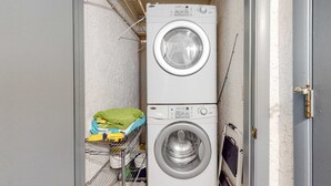 A laundry room with two stacked washing machines, a drying rack with folded clothes, and a shelf with cleaning supplies. - Beachfront Townhouse w/ Modern Upgrades Shared Pool, Fast WiFi, Outdoor Shower (Panama City Beach)