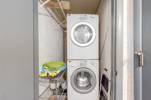 A laundry room with two stacked washing machines, a drying rack with folded clothes, and a shelf with cleaning supplies. - Beachfront Townhouse w/ Modern Upgrades Shared Pool, Fast WiFi, Outdoor Shower (Panama City Beach)