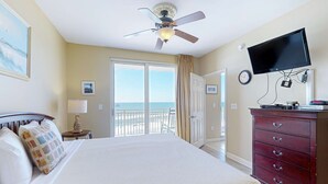 Ein Hotelzimmer mit Bett, Deckenventilator, Wandfernseher, Kommode und Meerblick durch die Balkontüren.