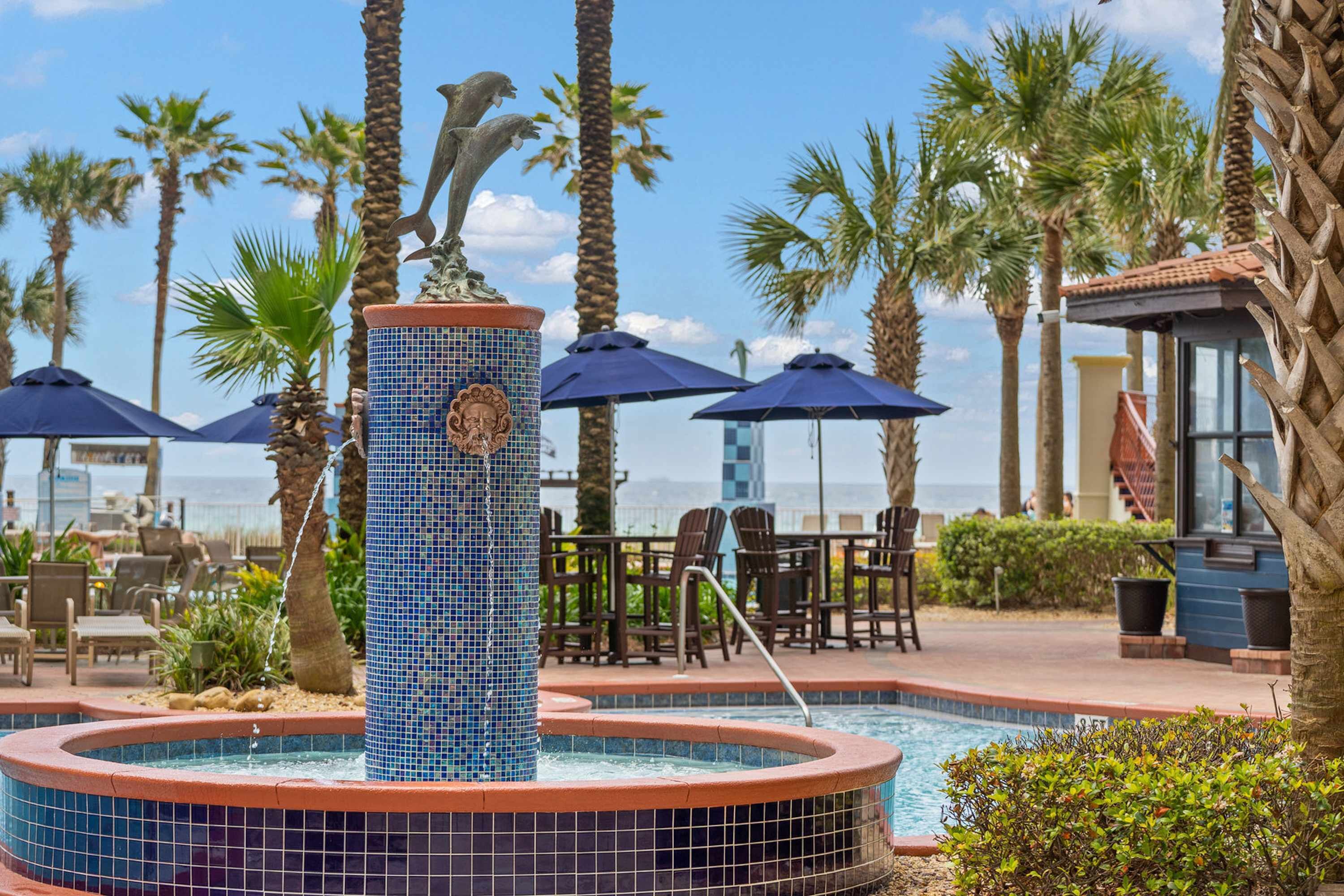 A pool area with a dolphin statue, palm trees, and outdoor seating.