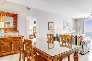 Una sala de estar moderna con una mesa de comedor de vidrio, sillas de madera, un sofá colorido a rayas y un espejo grande.