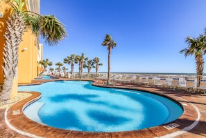 Una piscina de diseño curvo, rodeada de palmeras y sillones de descanso, con vistas despejadas al océano de fondo.