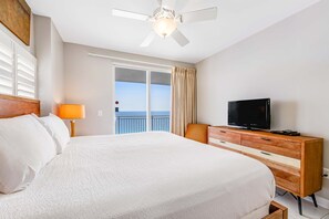 Habitación de hotel con una cama grande, un televisor en una cómoda de madera, un ventilador de techo y un balcón con vistas.