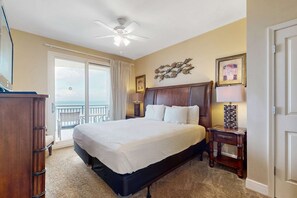 Une chambre avec un grand lit, un ventilateur de plafond, un balcon avec vue et une commode en bois.