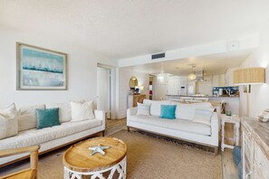 A spacious living room with two white sofas, a wooden coffee table, and a large painting on the wall.