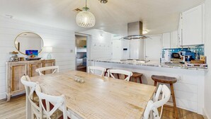 Une cuisine moderne avec des meubles blancs, une table à manger en bois et un luminaire suspendu.
