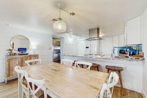Une cuisine moderne avec des meubles blancs, une table à manger en bois et un luminaire suspendu.