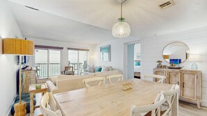 Un vaste espace dédié à la salle à manger, avec une table en bois et des chaises blanches, un luminaire suspendu et une vue sur le balcon.