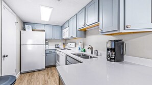 A compact kitchen with white appliances, grey cabinets, and a coffee maker. - Beautiful Pinnacle Port condo with pools & basketball court right next to beach (Panama City Beach)