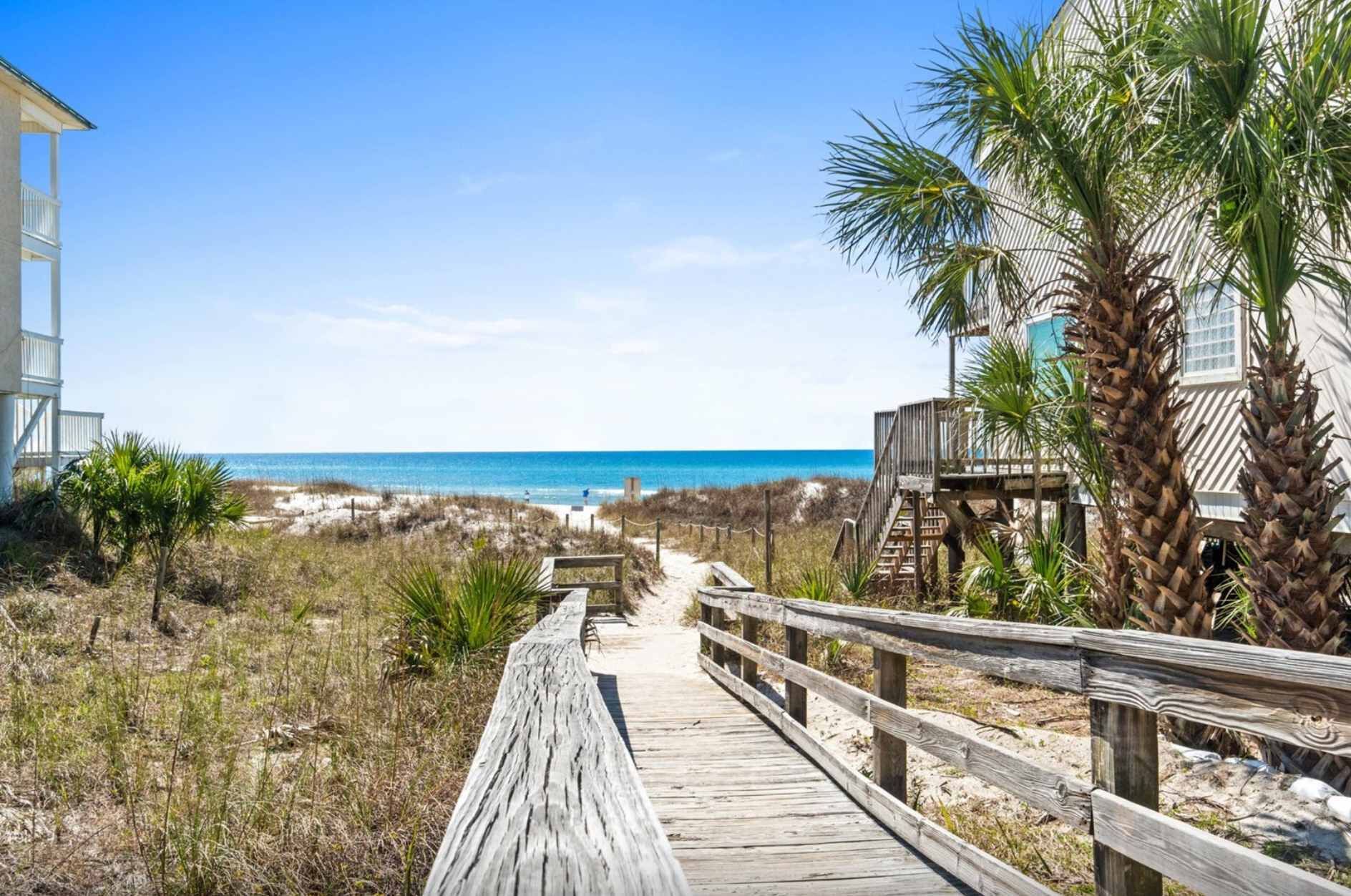 A wooden boardwalk leading to a beach with a clear view of the ocean.