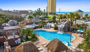 A resort with a swimming pool, lounge chairs, palm trees, and a view of the ocean and city skyline. - Renovated Townhome with Central AC, Shared Pools & Hot Tubs–Minutes to Beach (Panama City Beach)