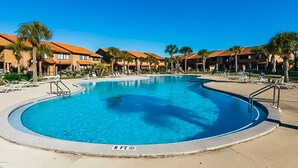 Une piscine entourée de palmiers et de bâtiments d’hôtel, sous un ciel d’un bleu limpide.