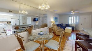 Un salon moderne avec une table à manger en verre, des chaises en osier, un canapé et un ventilateur de plafond.