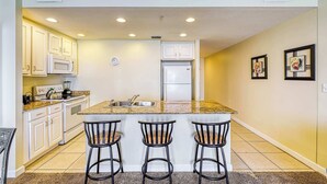 A kitchen with white cabinets, a granite countertop, a sink, and three bar stools.