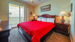 A hotel room with a large bed, a ceiling fan, a nightstand with a lamp, and a view through the glass doors.