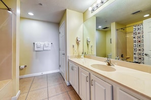A bathroom with a beige sink, a large mirror, and a shower curtain. - Beach getaway steps from the beach with pool & gym (Panama City Beach)