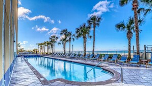 A swimming pool with blue tiles, surrounded by palm trees and blue lounge chairs. - Waterfront condo with grills, pool & fitness center - walk to the beach (Panama City Beach)