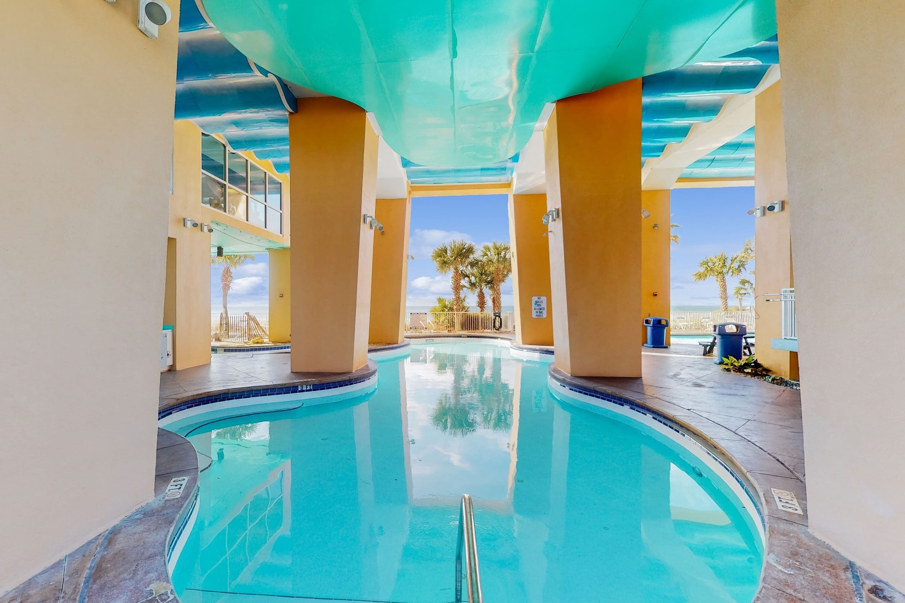 Une piscine à l’eau d’un bleu cristallin, entourée de murs de couleur beige et soutenue par des colonnes.