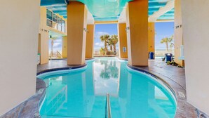 A swimming pool with clear blue water, surrounded by beige walls and supported by columns. - Beachfront, high-end condo with Pool, Hot tub & Splash pad (Panama City Beach)