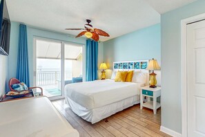 A bedroom with a bed, two bedside lamps, a ceiling fan, a window with curtains, and a view of the outside. - Beachfront Paradise, huge balcony, panoramic Gulf views, pool & fitness room (Panama City Beach)