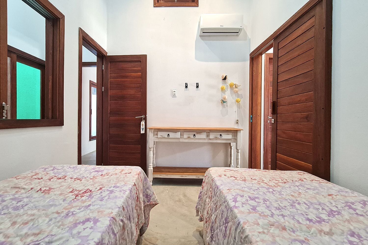 Un dormitorio con dos camas, un escritorio de madera, un aire acondicionado instalado en la pared y una puerta con cerradura.