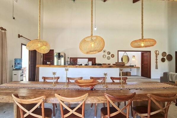 A spacious dining area with a large wooden table, multiple chairs, and hanging woven light fixtures.