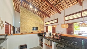 A kitchen with a stone wall, wooden ceiling, and a black countertop. - Chales em Jericoacoara by Carpediem (Jijoca de Jericoacoara)