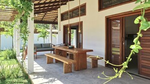 An outdoor patio with a wooden table and benches, surrounded by greenery and a pergola. - Chales em Jericoacoara by Carpediem (Jijoca de Jericoacoara)