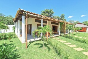 A modern house with a covered porch, a stone wall, and a well-maintained garden with palm trees and stepping stones.