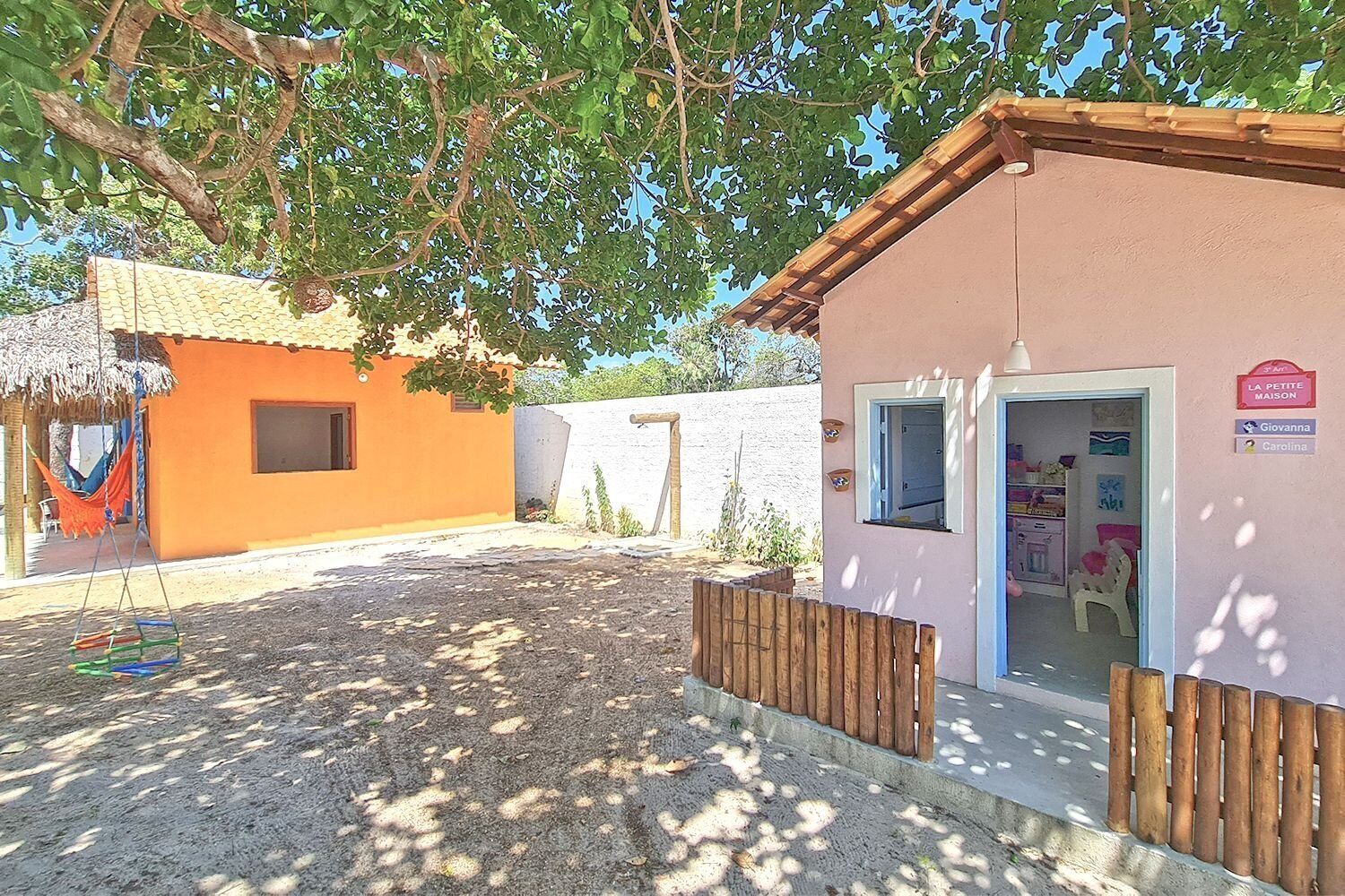 A small building with a pink exterior and a wooden fence. There is a hammock and a swing in the foreground.