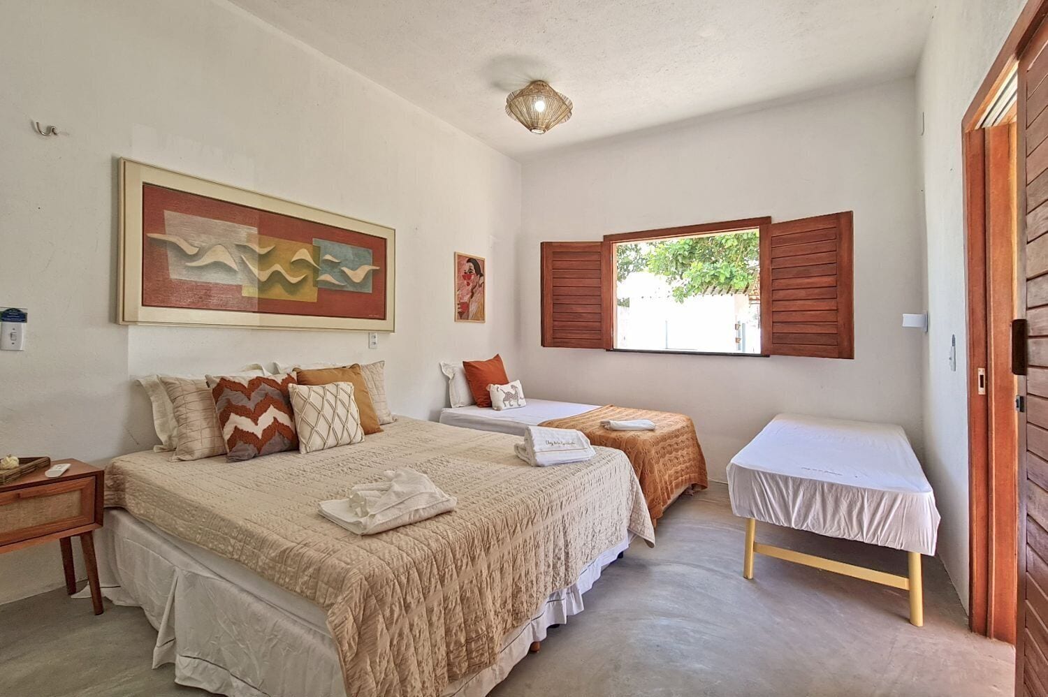 Un dormitorio con dos camas, una mesita y un ventanal con contraventanas.