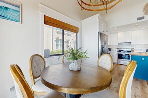 Een eetruimte met een ronde houten tafel, witte stoelen met bekleding en een vaas met groene planten.