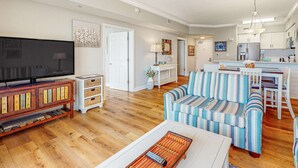 A spacious living room with a television, a striped sofa, and a coffee table. - Picturesque 18th-floor gulf-front condo w/ pools, hot tubs & beach service (Panama City Beach)