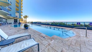 A pool area with lounge chairs, a clear sky, and a building with balconies. - 7th-floor resort studio with partial Gulf views, outdoor pool, gym & hot tub (Panama City Beach)