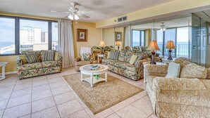 A spacious living room with two sofas, a coffee table, and a view of the ocean through large windows. - Centrally located condo w/ private balcony, Pool & Hot tub (Panama City Beach)