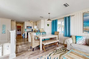 Amplia sala de estar con mesa de comedor, sillas de mimbre, un sofá y una cocina al fondo.