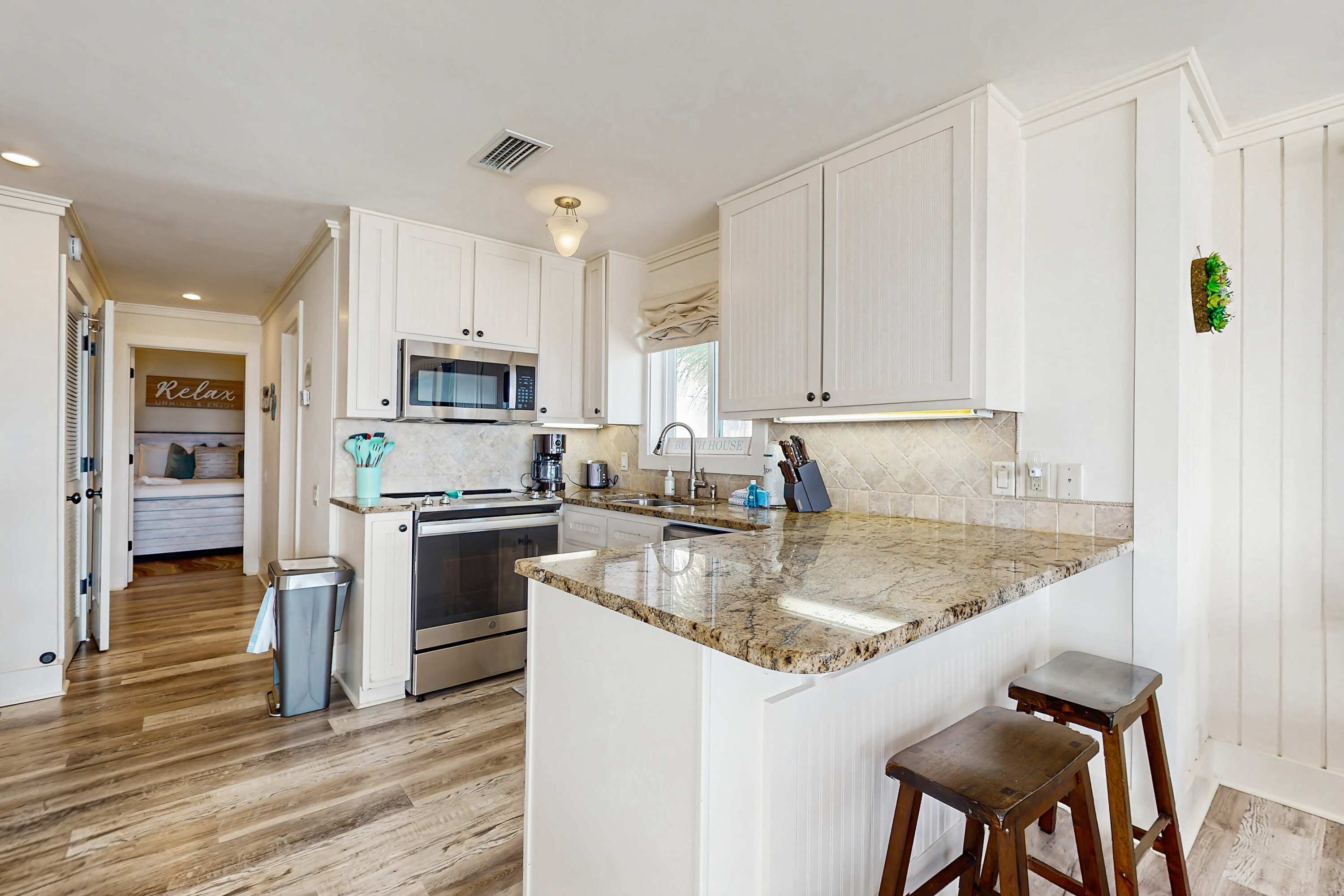 A modern kitchen with white cabinetry, a granite countertop, and a stainless steel range hood.
