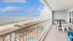 Un balcon avec vue sur la plage et l’océan, une piscine et une table avec des chaises.