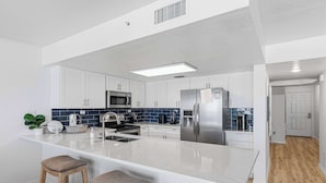 Une cuisine moderne avec des meubles blancs, un îlot central, des appareils en acier inoxydable et un pare-feu bleu.