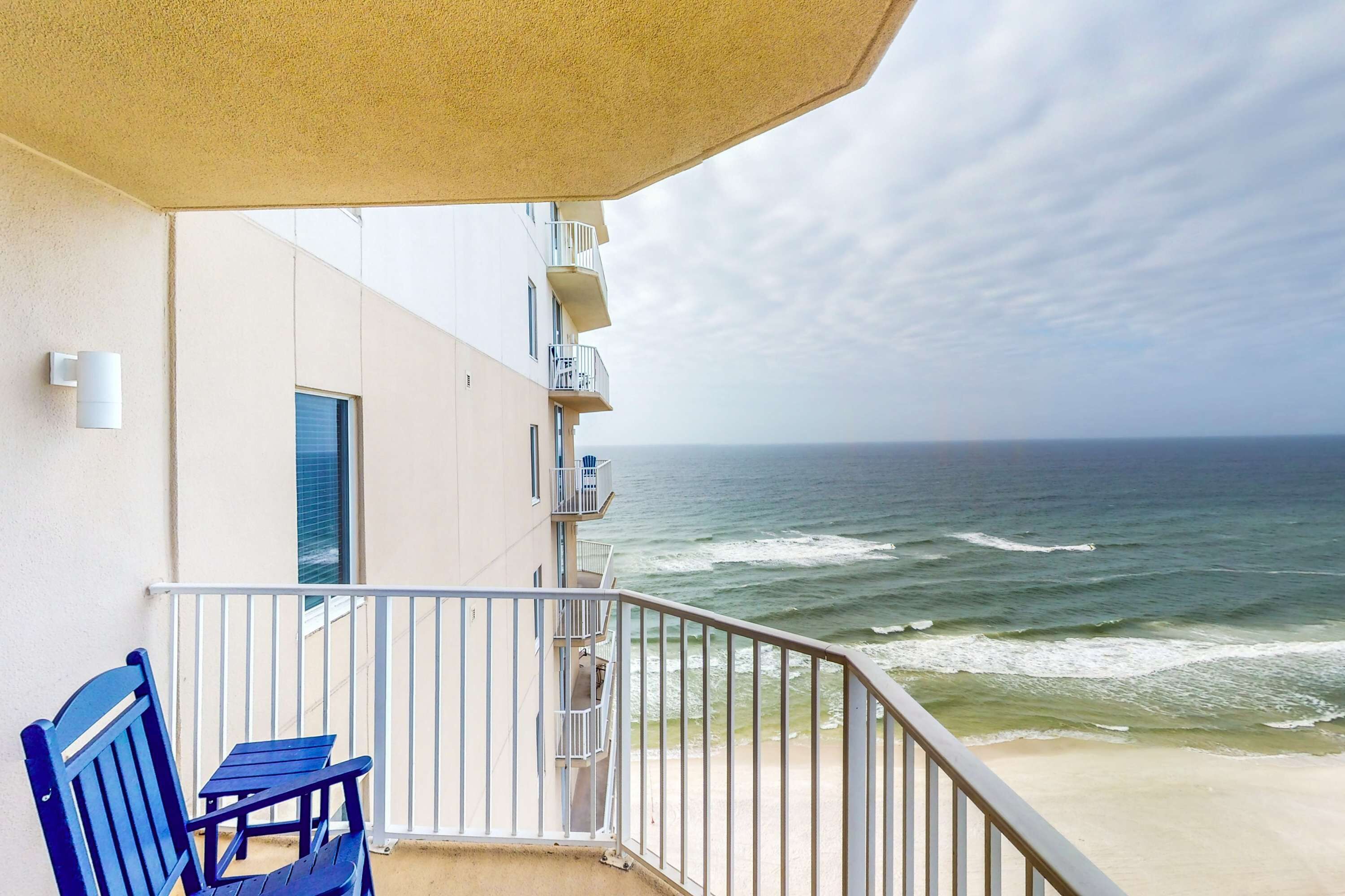 A balcony with a view of the ocean, a chair, and a small table.
