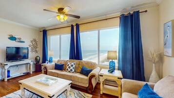 A living room with a large window, a ceiling fan, a television, and a sofa with blue cushions.