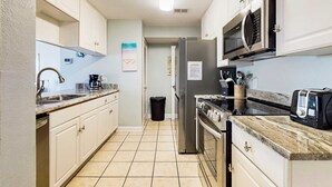 A modern kitchen with white cabinets, a stainless steel refrigerator, a microwave, a stove, and a coffee maker. - Adorable condo across from the Gulf with central AC, deck, pool & grill (Perdido Key)