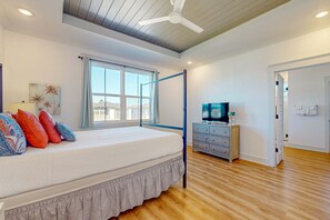 Ein Schlafzimmer mit einem Bett, einem Fernseher, einem Deckenventilator, einem Fenster und Holzboden.