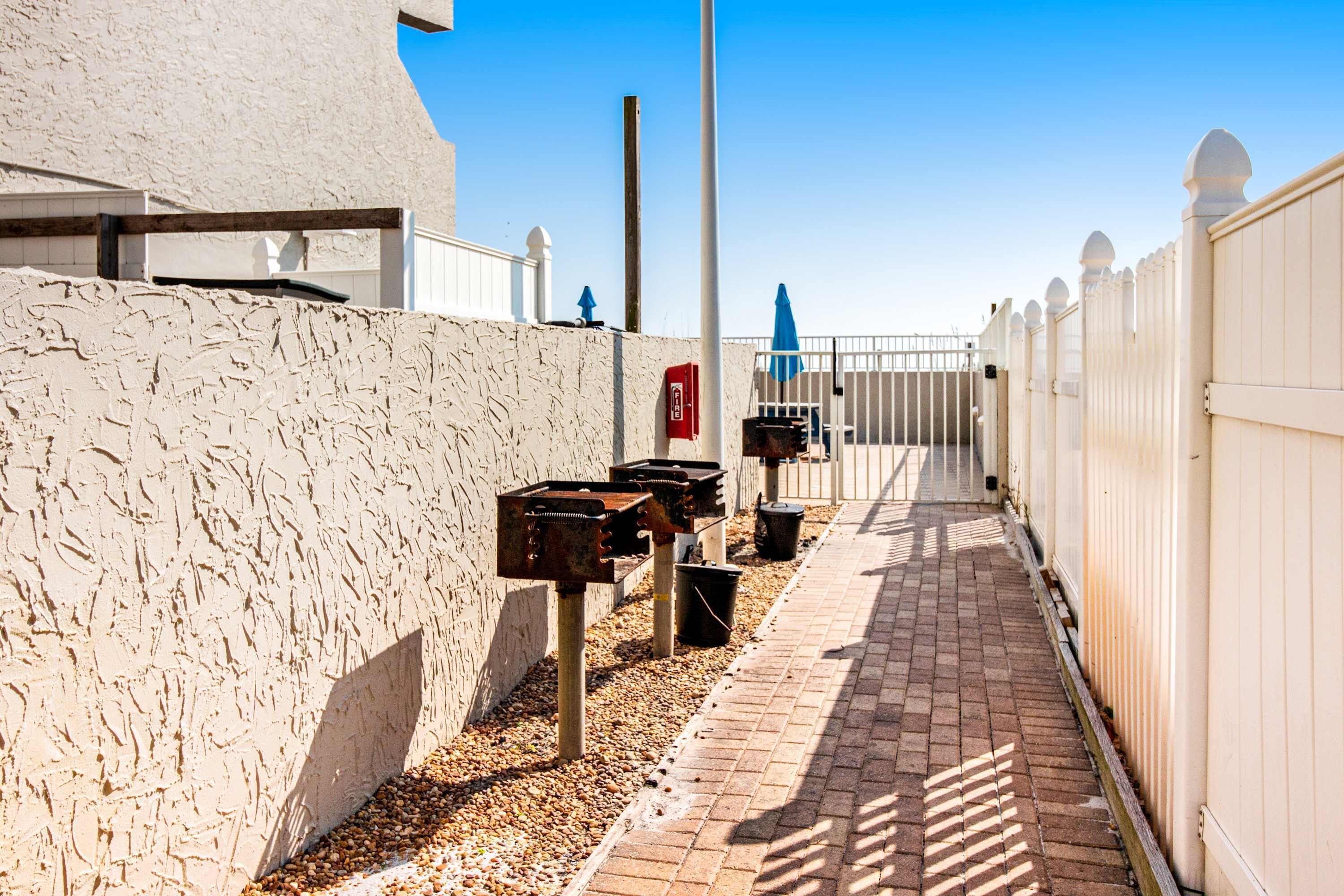 Un étroit sentier bordé d’un côté par un mur blanc et de l’autre par une clôture, qui mène à un portail.