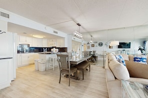 A spacious living area with a dining table, chairs, and a sofa. - Beachfront condo with pool & tennis courts - quick drive to dining (Fort Walton Beach)