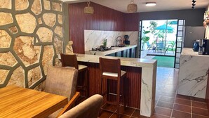 A modern kitchen with a marble countertop, wooden chairs, and a stone wall. - Casa Vacaional (Bacalar)
