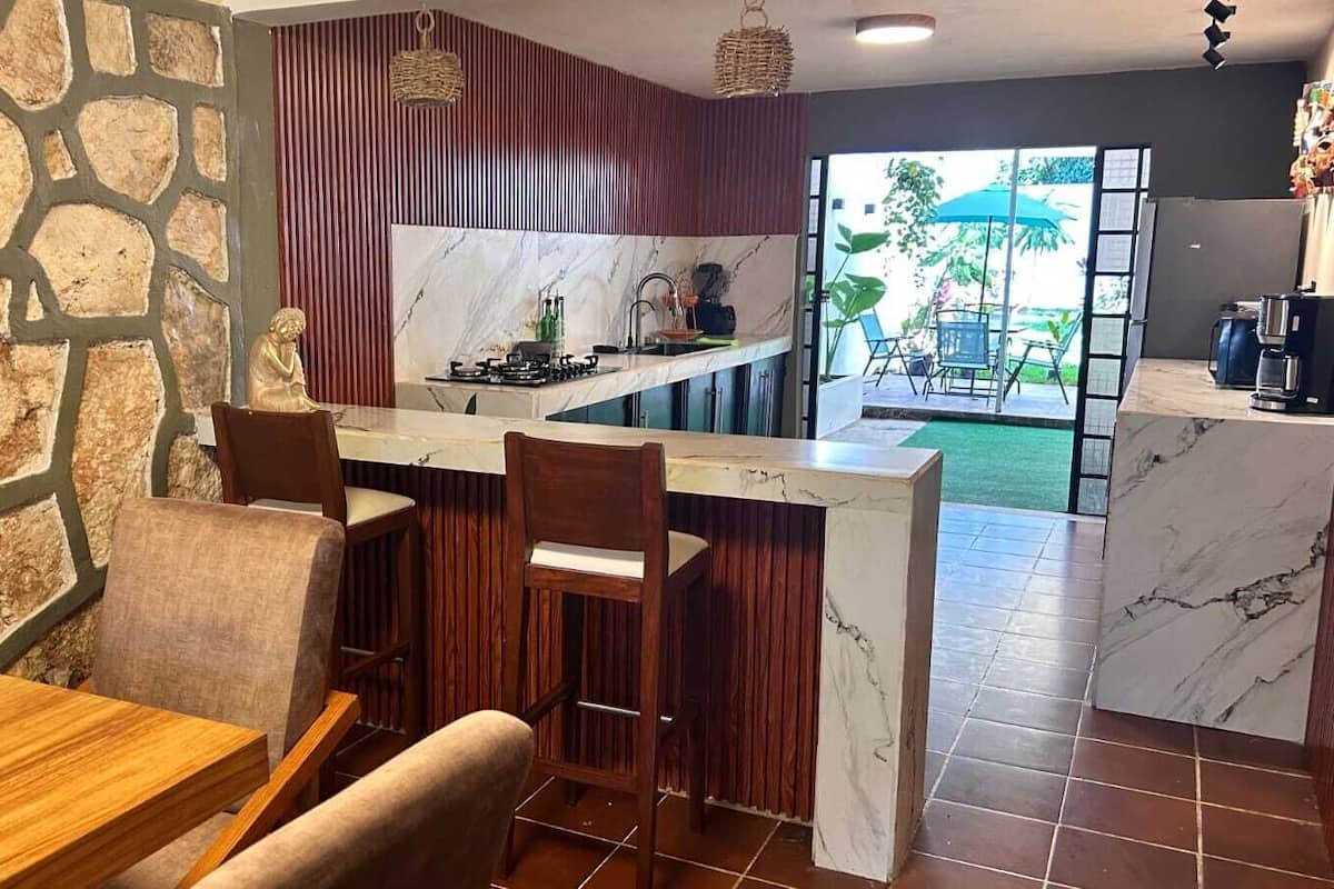 A modern kitchen with a marble countertop, wooden chairs, and a stone wall.