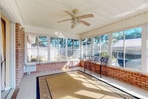 A sunroom with a ceiling fan, large windows, a brick wall, and a tiled floor. - Inviting dog-friendly home with pool, hot tub, enclosed yard, & W/D (Perdido Key)